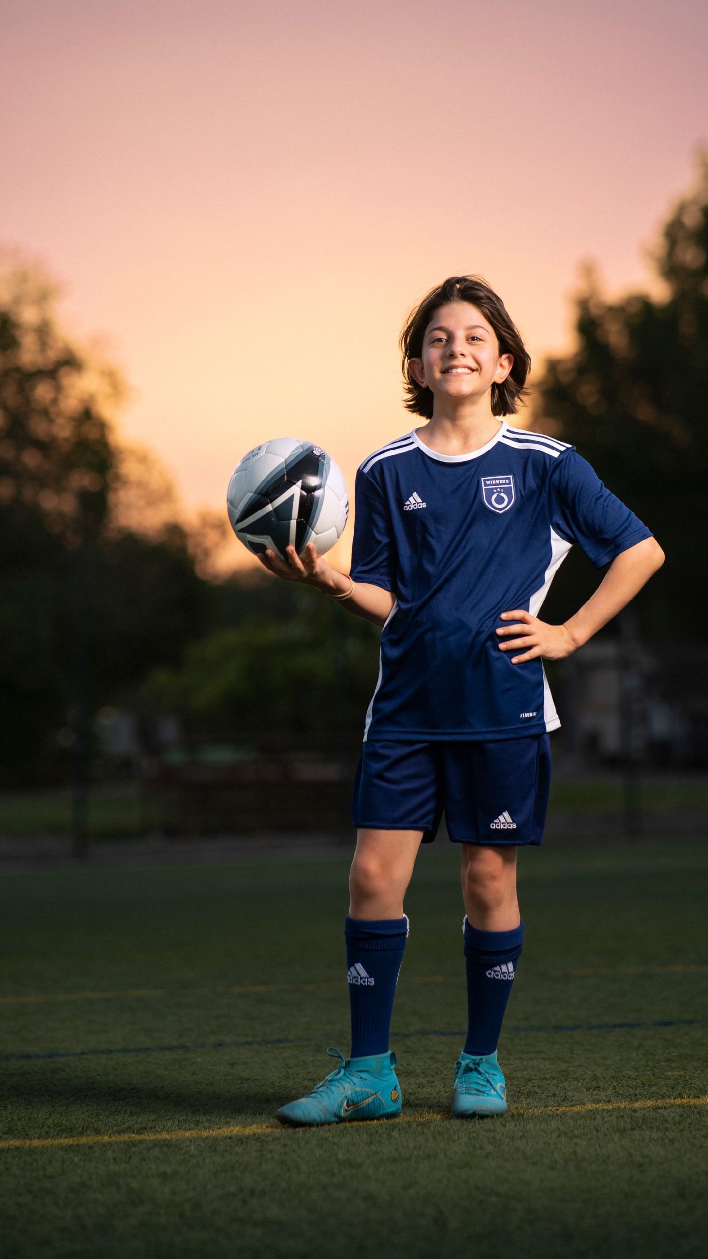 Young soccer player in team uniform holding a ball at sunset